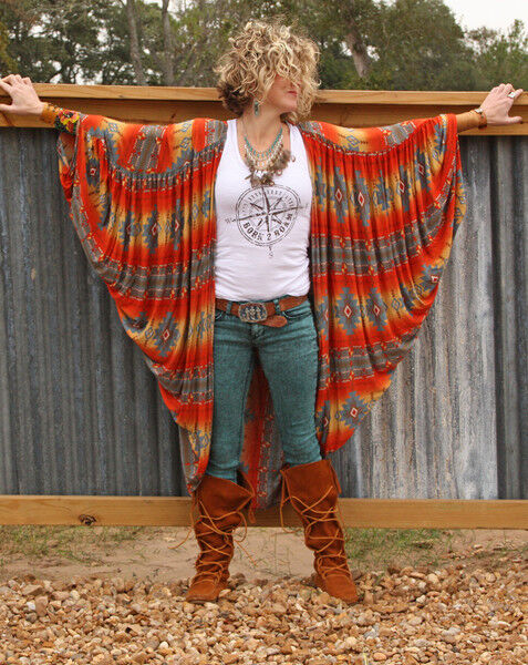 Blonde woman with short curly hair and warms extended wearing a colorful shawl, white tanktop, jeans and rustic leather boots