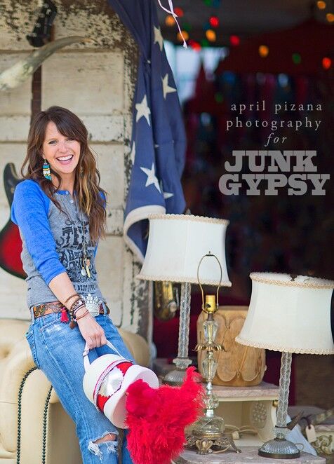 Lady in jeans and a blue graphic baseball shirt sitting on the arm of a leather chair near tables with lamps