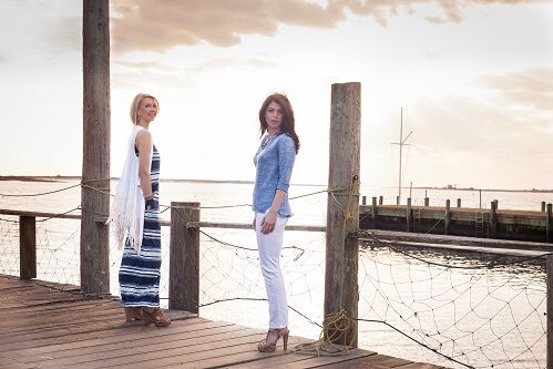 Two caucasian female models on a pier modeling East Coast fashion styles in front of a vast sky