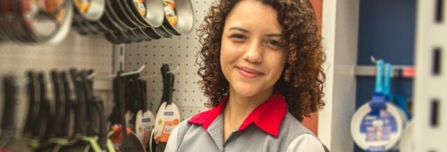 Woman store associate with brown curly hair wearing a grey collared shirt with bright red collars.